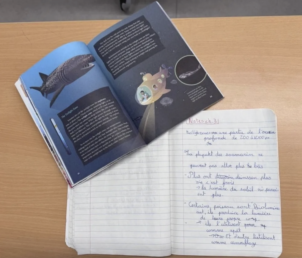Student notes in French beside an English-language science book, showing multilingual learning across languages
